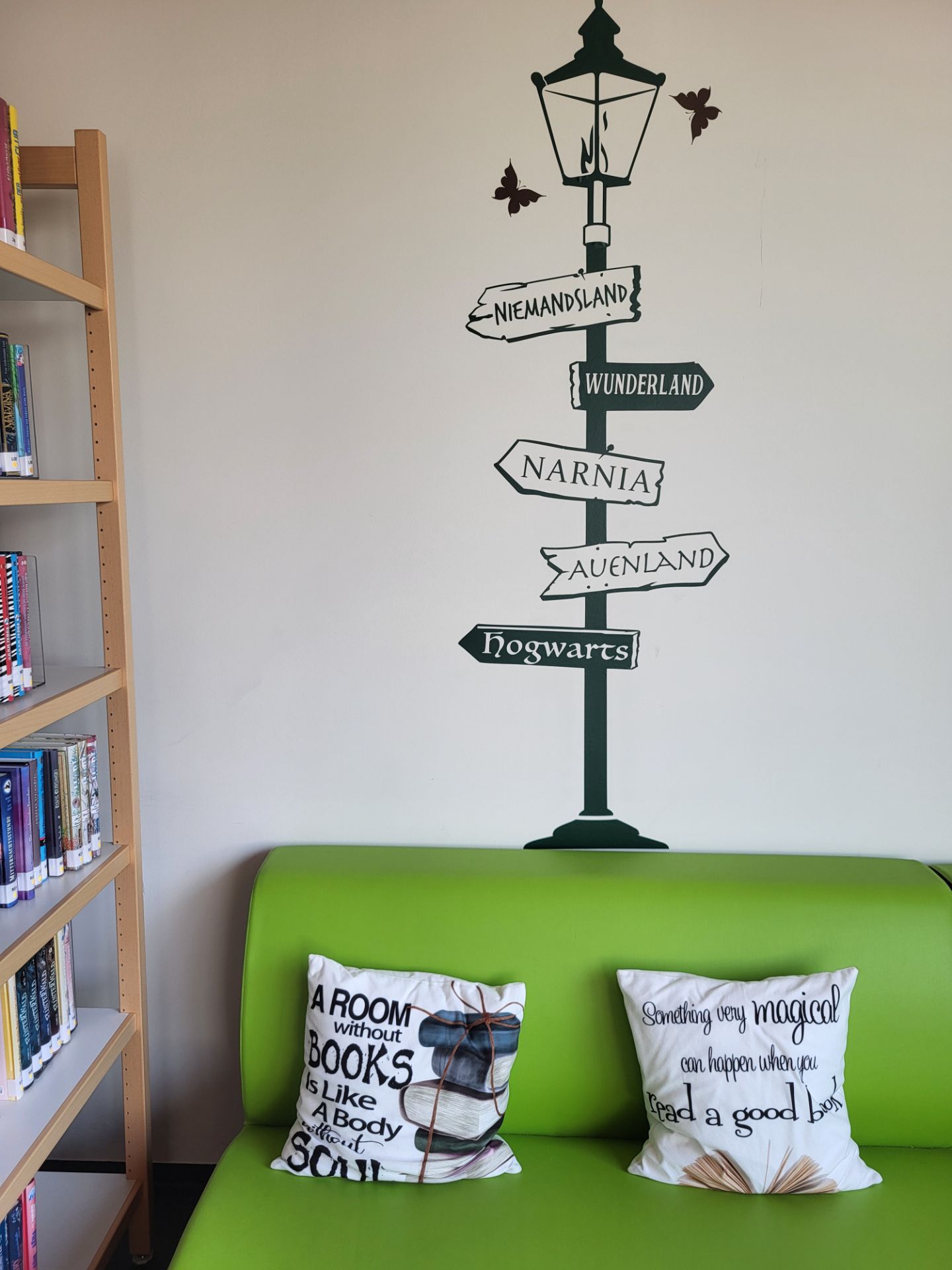 Leseecke mit grünem Sofa und Wegweiser-Wandtattoo nach Narnia, Hogwarts und ins Auenland